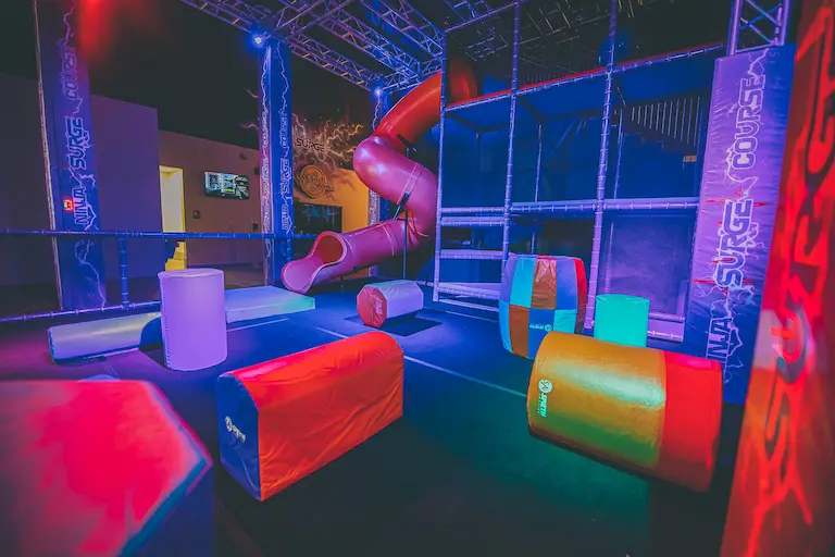 A vibrant indoor obstacle course with soft padded structures, slides, and climbing elements at Extreme Attractions, illuminated by colorful lights.