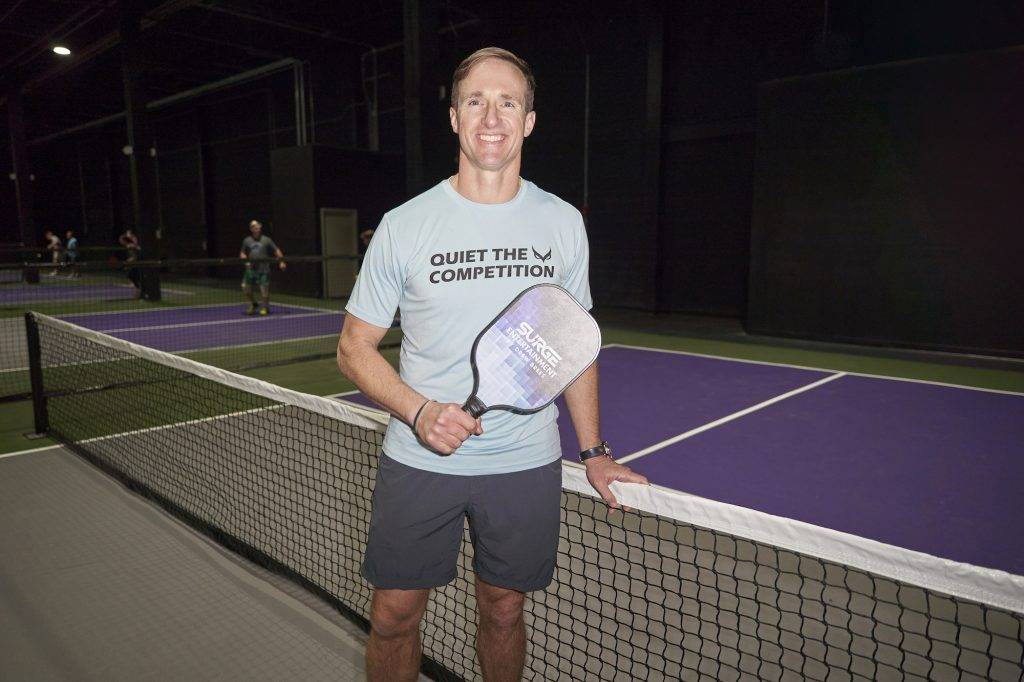 Drew Brees holds a Pickleball paddle on an indoor court, ready for a fun and competitive game.